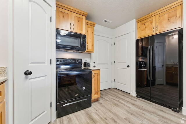 kitchen featuring light wood finished floors, visible vents, black appliances, light brown cabinetry, and a textured ceiling