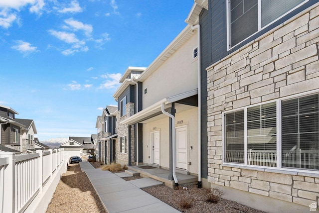 view of property exterior featuring fence, stone siding, a residential view, and stucco siding