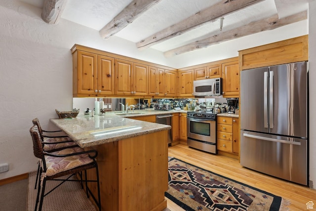 kitchen featuring beam ceiling, a sink, stainless steel appliances, a peninsula, and a textured wall