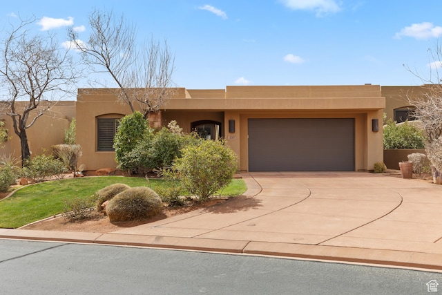 pueblo-style house featuring stucco siding, a front yard, a garage, and driveway
