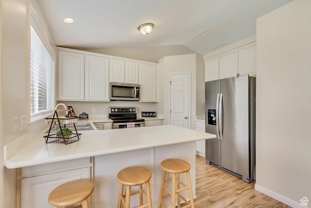 kitchen featuring light wood finished floors, stainless steel appliances, a peninsula, a sink, and lofted ceiling