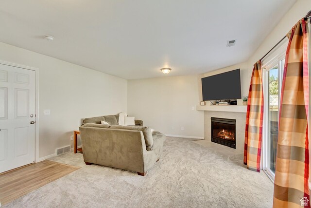 living room featuring a fireplace with flush hearth, carpet, visible vents, and baseboards
