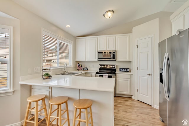 kitchen featuring a sink, light wood finished floors, white cabinets, a peninsula, and appliances with stainless steel finishes