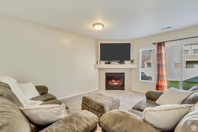 living room with a tiled fireplace, visible vents, baseboards, and light colored carpet