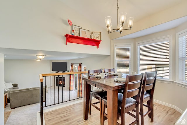 dining space with light wood-style floors, a warm lit fireplace, baseboards, and an inviting chandelier