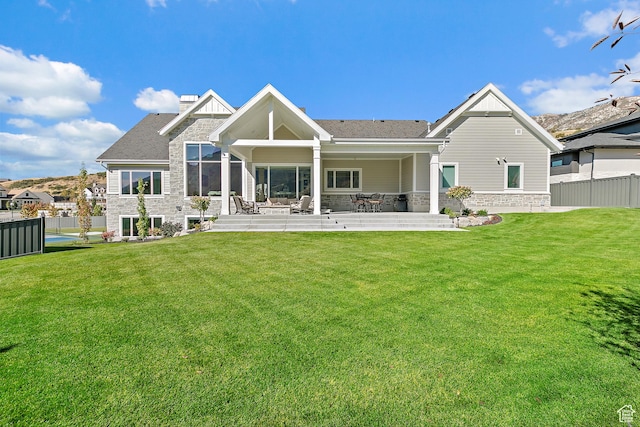 rear view of house with fence, a lawn, a chimney, a patio area, and stone siding