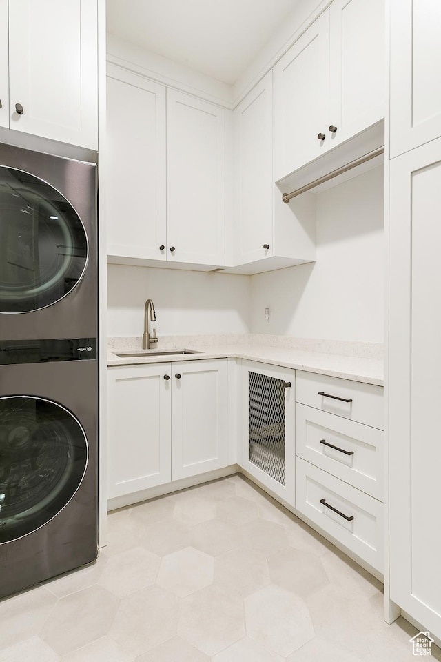 clothes washing area with cabinet space, stacked washer and clothes dryer, and a sink