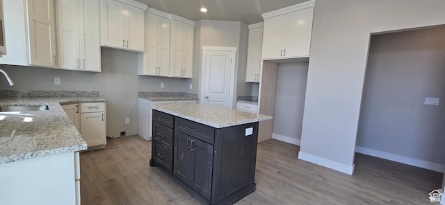 kitchen with white cabinets, light wood-style floors, light stone counters, and a sink