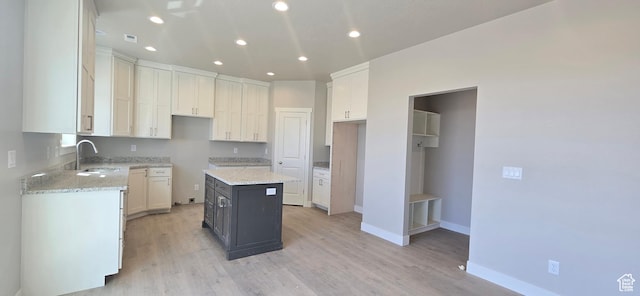 kitchen featuring a sink, light wood-type flooring, baseboards, a kitchen island, and light stone counters