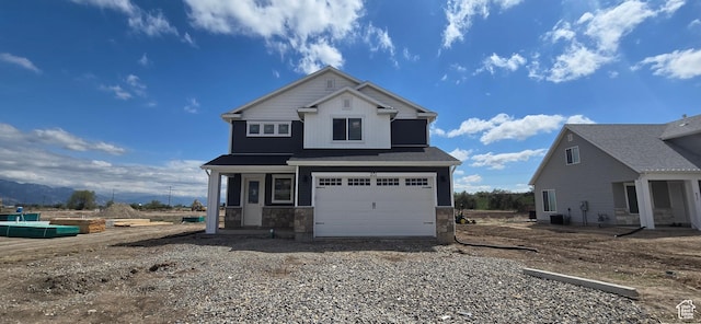 view of front of home with central AC unit, an attached garage, stone siding, and gravel driveway