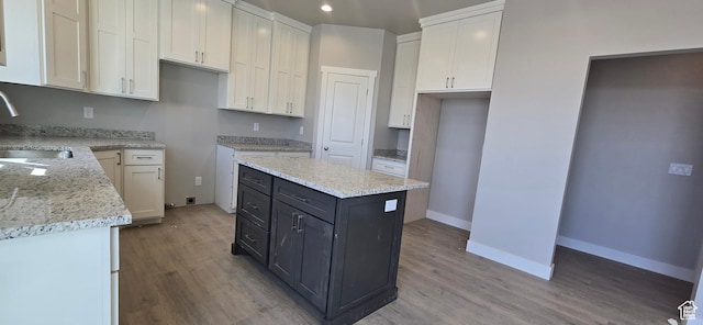 kitchen featuring a sink, light wood-style flooring, white cabinetry, a center island, and baseboards