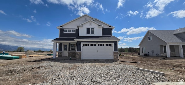 view of front of property with gravel driveway, stone siding, an attached garage, and board and batten siding