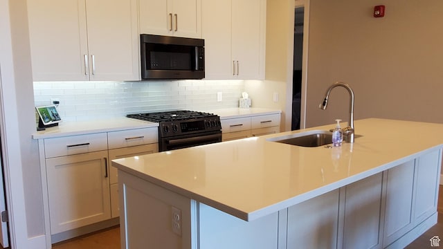 kitchen featuring tasteful backsplash, stainless steel microwave, a sink, gas range, and a kitchen island with sink