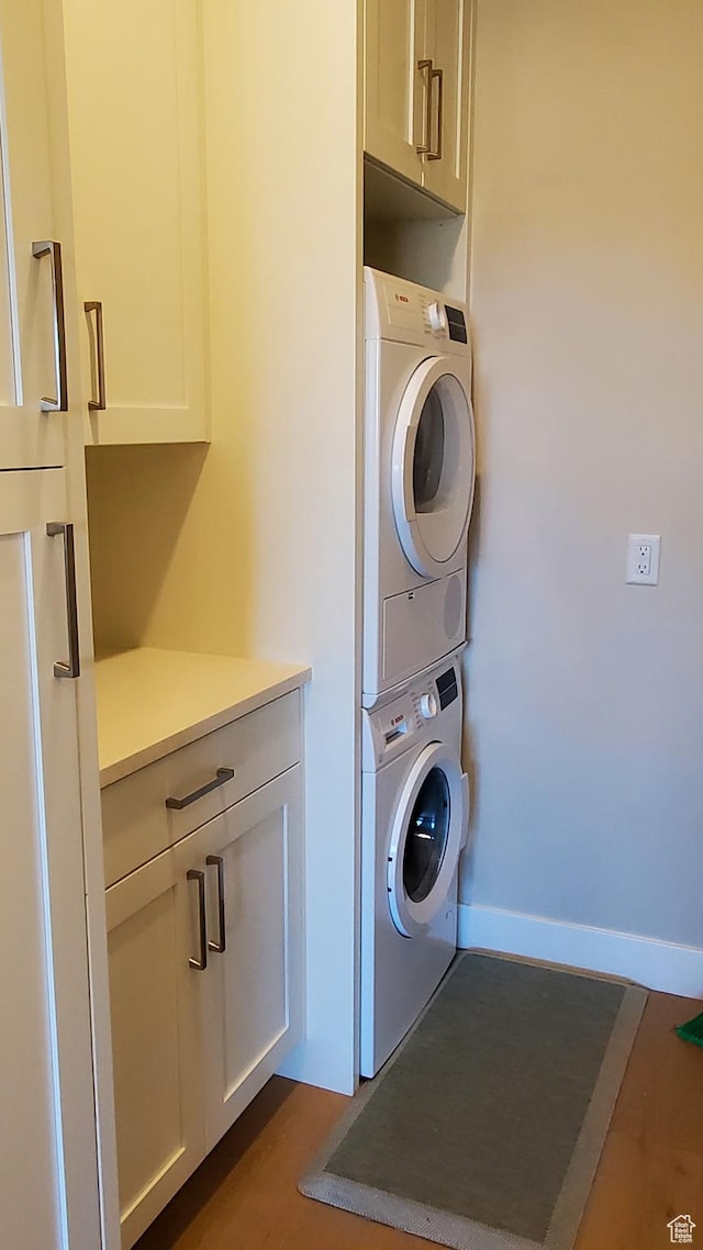 washroom with baseboards, cabinet space, and stacked washer and clothes dryer
