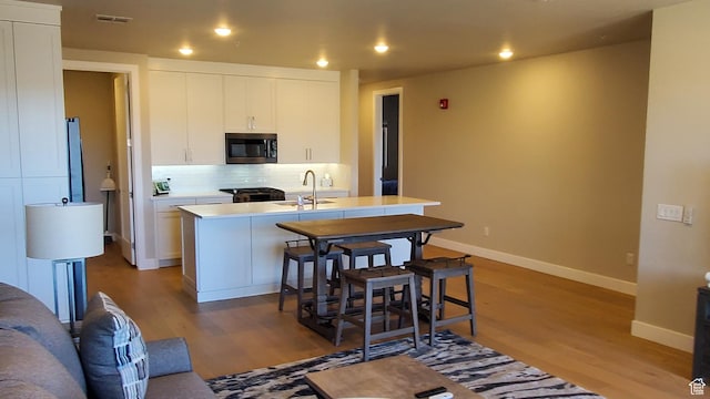 kitchen with tasteful backsplash, stainless steel microwave, an island with sink, wood finished floors, and a sink