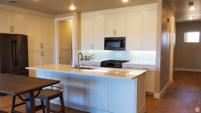 kitchen with decorative backsplash, wood finished floors, gas stove, white cabinetry, and a sink