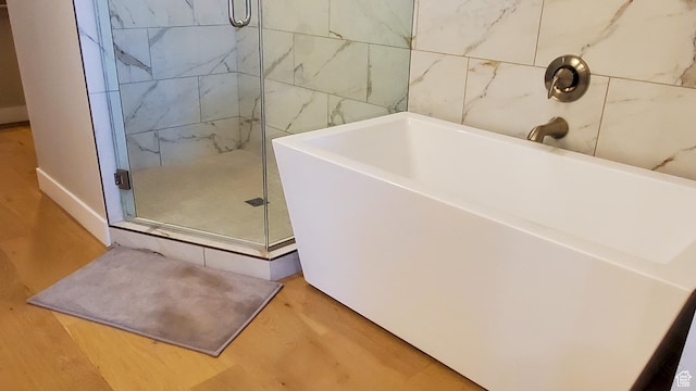 full bathroom featuring a bathing tub, a shower stall, and wood finished floors