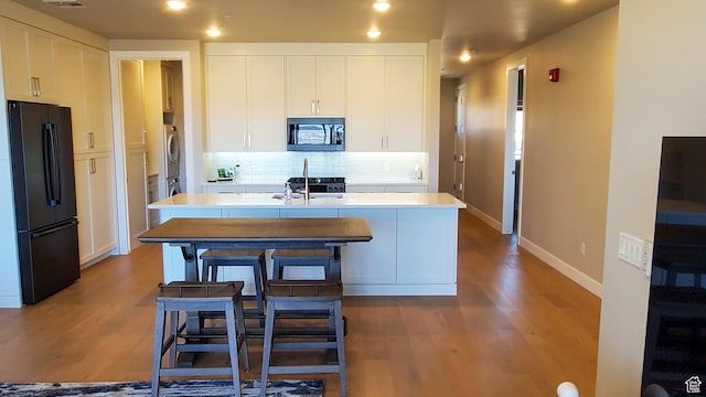 kitchen with decorative backsplash, an island with sink, wood finished floors, and freestanding refrigerator