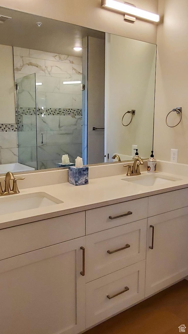 full bath featuring a marble finish shower, double vanity, and a sink