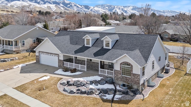 view of front of home with a porch, concrete driveway, roof with shingles, a mountain view, and an attached garage