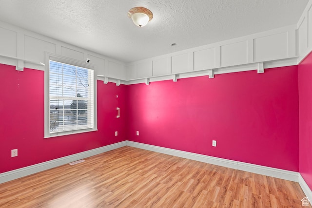 unfurnished room with visible vents, light wood-style flooring, a textured ceiling, and baseboards