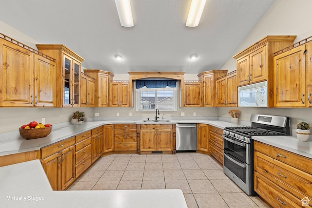 kitchen with glass insert cabinets, light countertops, light tile patterned floors, stainless steel appliances, and a sink