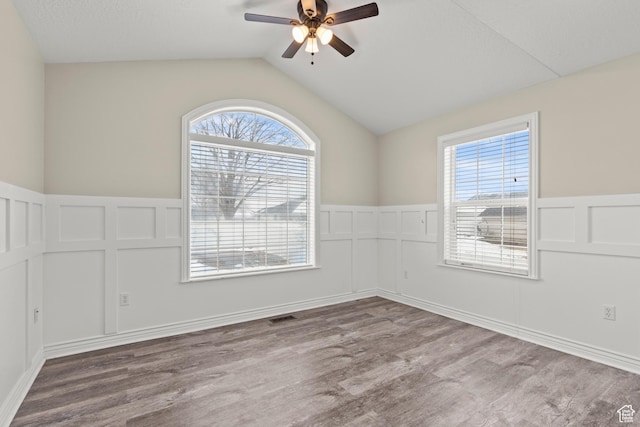 unfurnished room featuring visible vents, a wainscoted wall, a ceiling fan, wood finished floors, and vaulted ceiling