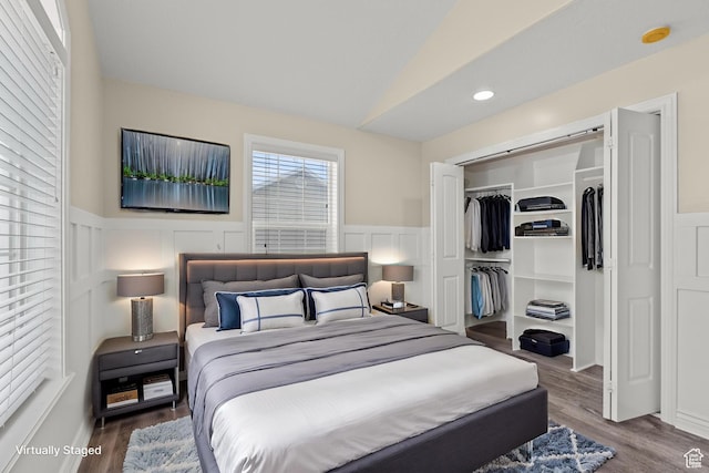 bedroom with lofted ceiling, wood finished floors, a closet, and wainscoting