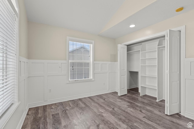 unfurnished bedroom featuring a closet, wainscoting, lofted ceiling, and wood finished floors