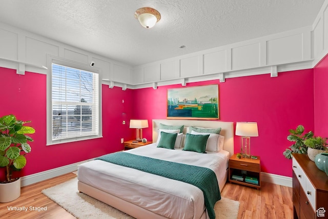 bedroom with light wood finished floors, a textured ceiling, and baseboards