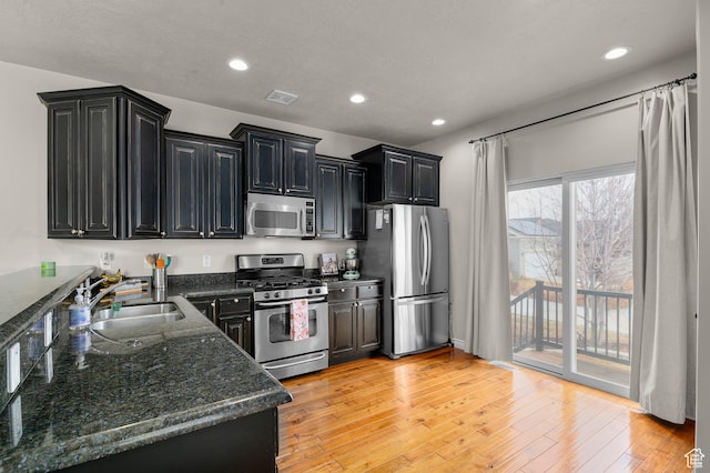 11709 S Grandville Ave, South Jordan, UT 84009 - kitchen featuring appliances with stainless steel finishes, dark cabinetry, recessed lighting, light wood finished floors, and dark stone counters