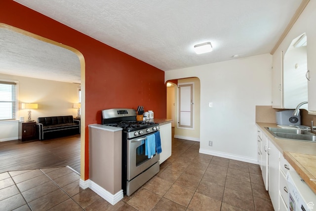 2348 Iowa Ave, Ogden, UT 84401 - kitchen featuring light countertops, stainless steel gas range, light tile patterned floors, arched walkways, and white cabinetry