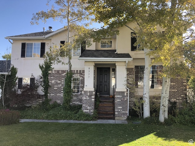 view of front of house featuring a front yard, brick siding, and stucco siding