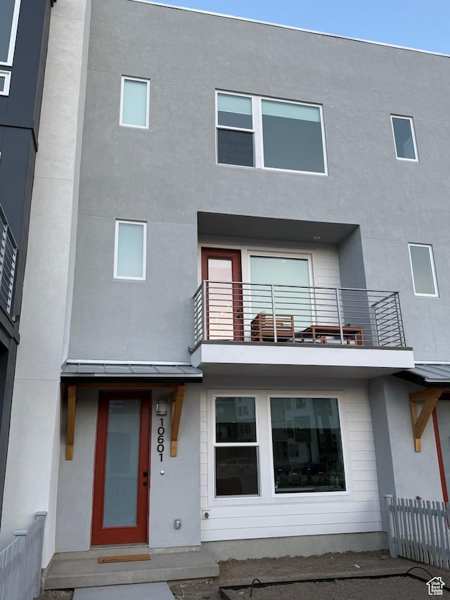 rear view of property featuring stucco siding, a balcony, and fence