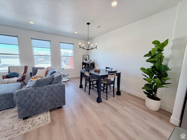 dining room featuring light wood finished floors, a textured ceiling, baseboards, and an inviting chandelier