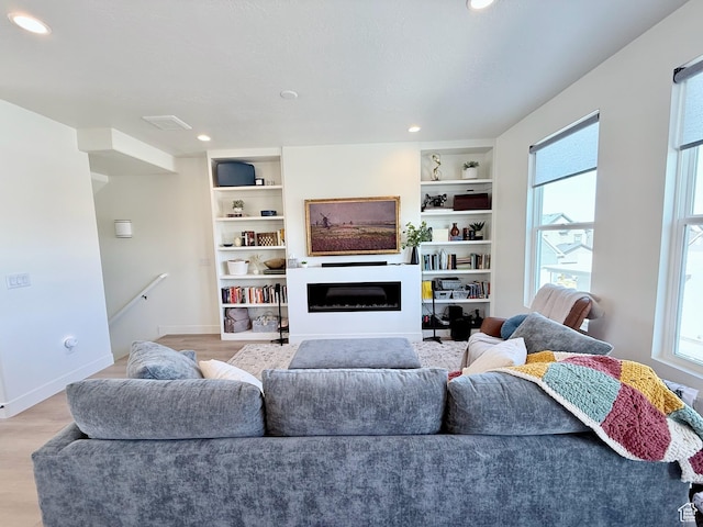 living room featuring built in features, baseboards, light wood-style flooring, and a fireplace
