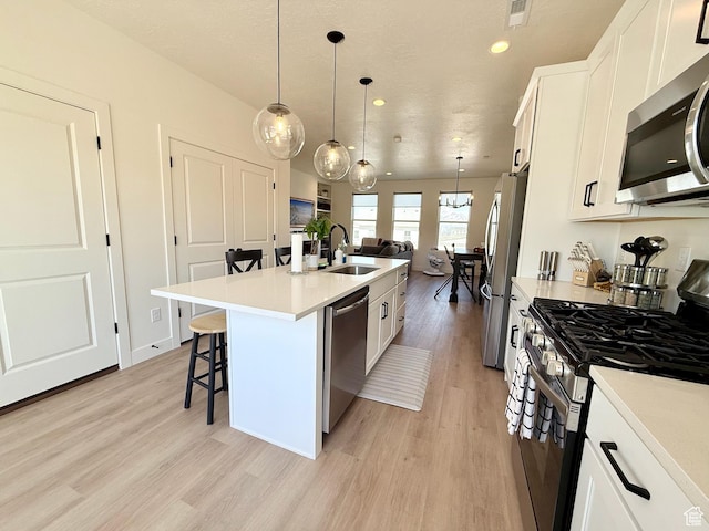 kitchen featuring a center island with sink, light wood-style flooring, a sink, stainless steel appliances, and a kitchen bar
