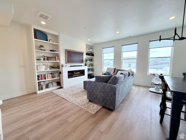 living room with baseboards, visible vents, light wood finished floors, recessed lighting, and a glass covered fireplace