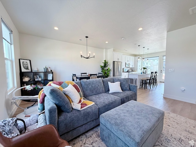 living room with baseboards, recessed lighting, light wood-type flooring, and a chandelier