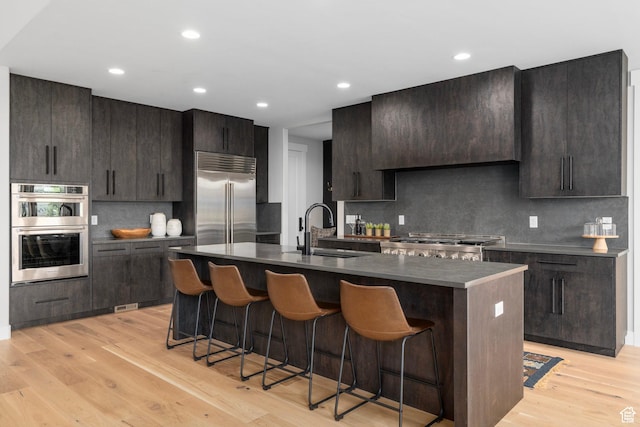 915 Farrell Farm Cir, Midway, UT 84049 - kitchen with range hood, appliances with stainless steel finishes, a kitchen breakfast bar, light wood-style floors, and a sink