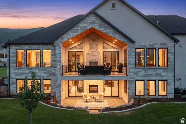 915 Farrell Farm Cir, Midway, UT 84049 - back of house at dusk with a patio area, stone siding, a yard, and a balcony