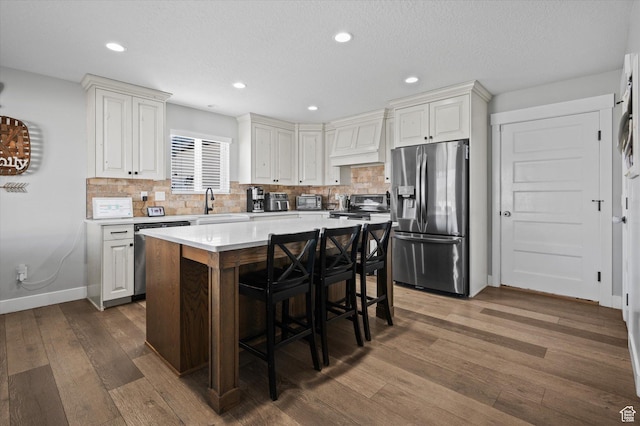 1490 N 4925 W, Plain City, UT 84404 - kitchen featuring dark wood-style floors, premium range hood, light countertops, appliances with stainless steel finishes, and a kitchen bar