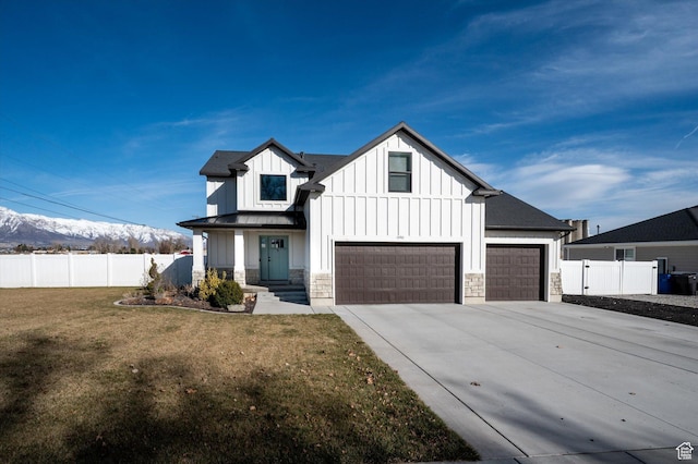 modern farmhouse style home featuring board and batten siding, a front lawn, fence, stone siding, and driveway