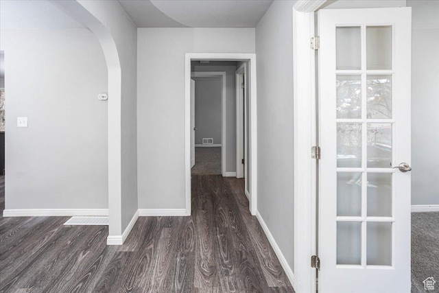 hallway with baseboards, arched walkways, visible vents, and wood finished floors