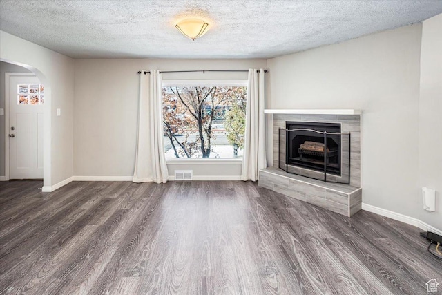 unfurnished living room featuring visible vents, arched walkways, baseboards, and wood finished floors