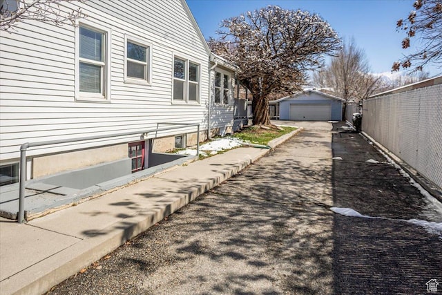view of side of home with a detached garage, an outdoor structure, driveway, and fence