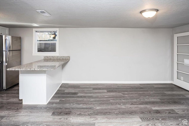 kitchen with a peninsula, light stone countertops, freestanding refrigerator, and dark wood-style flooring