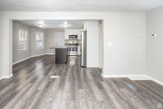 unfurnished living room featuring visible vents, baseboards, a textured ceiling, and dark wood finished floors