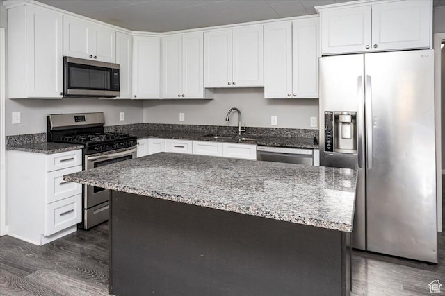 kitchen with a sink, dark wood finished floors, white cabinetry, dark stone counters, and appliances with stainless steel finishes
