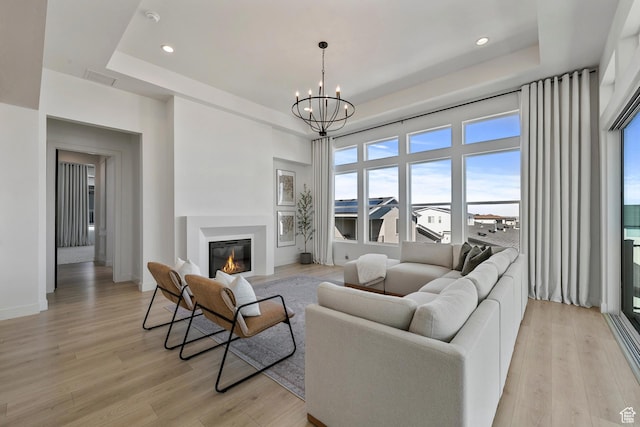 4784 W Juniper Bend Cir, Herriman, UT 84096 - living room featuring baseboards, a chandelier, a tray ceiling, light wood-style floors, and a glass covered fireplace